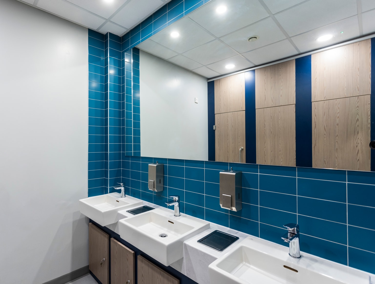 Image of bathroom sinks with toilet cubicles visible in the mirrors